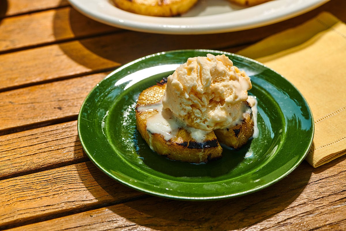 Grilled pineapple topped with vanilla ice cream on green plate.