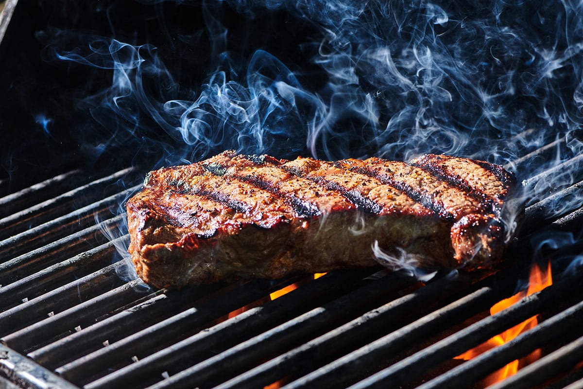 Rib-eye steak cooking on hot grill over flames.