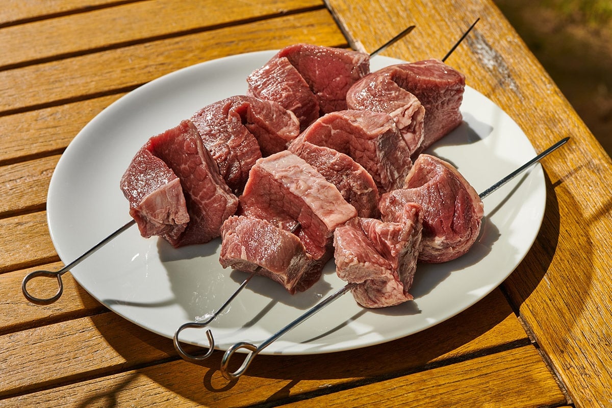 Raw slices of sirloin cap skewered on plate.