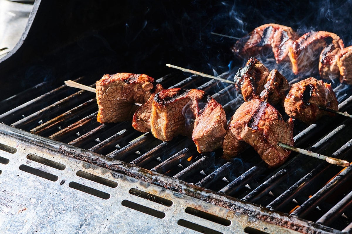Grilling skewered sirloin cap over flames.