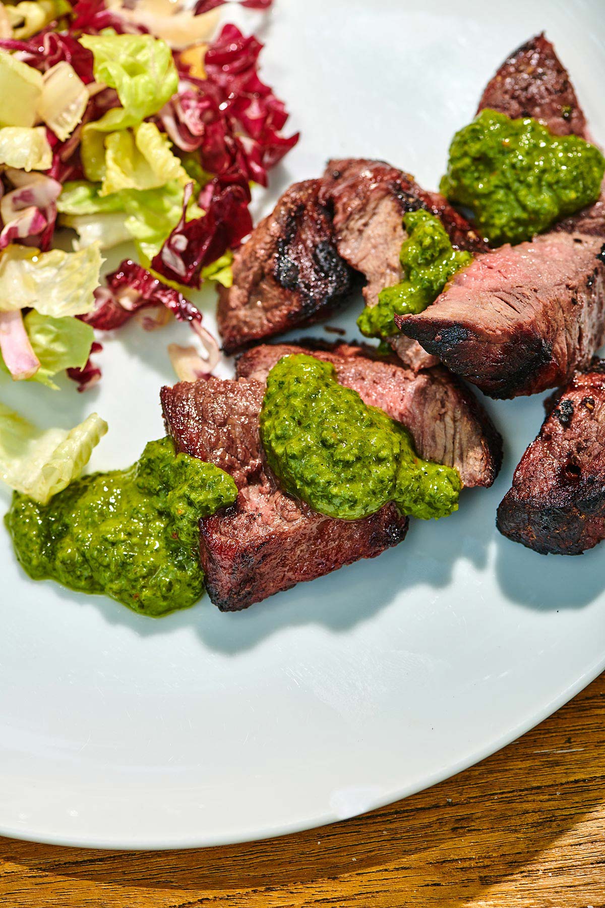 Slices of grilled sirloin cap with chimichurri sauce on white plate.
