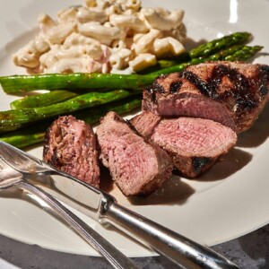 Grilled top sirloin steak and asparagus on plate with macaroni salad.