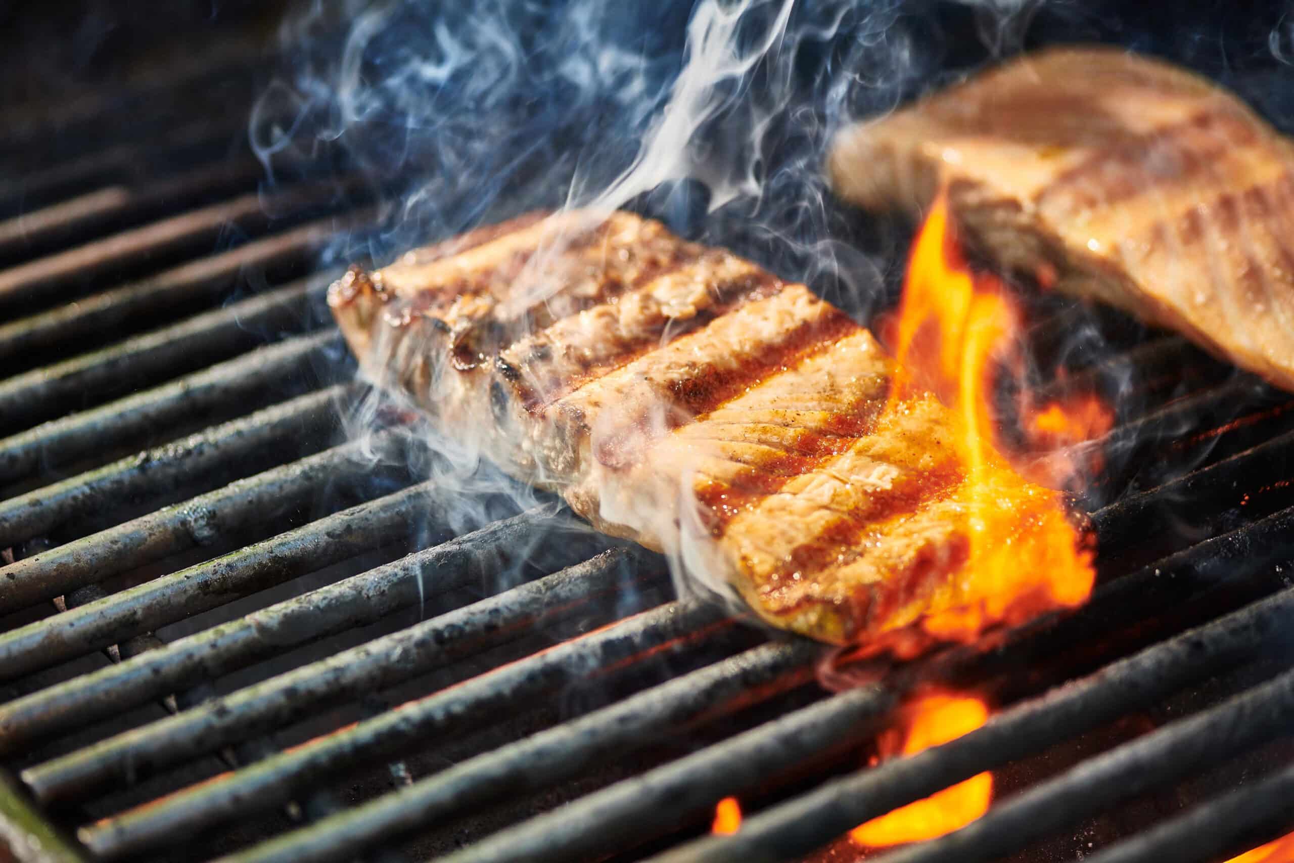 Salmon filets cooking on fiery grill.