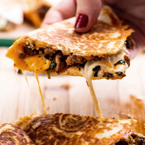Woman holding quesadilla slice over plate with gooey cheese.
