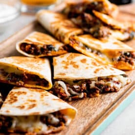 Beef and cheese quesadilla triangles on wood cutting board.
