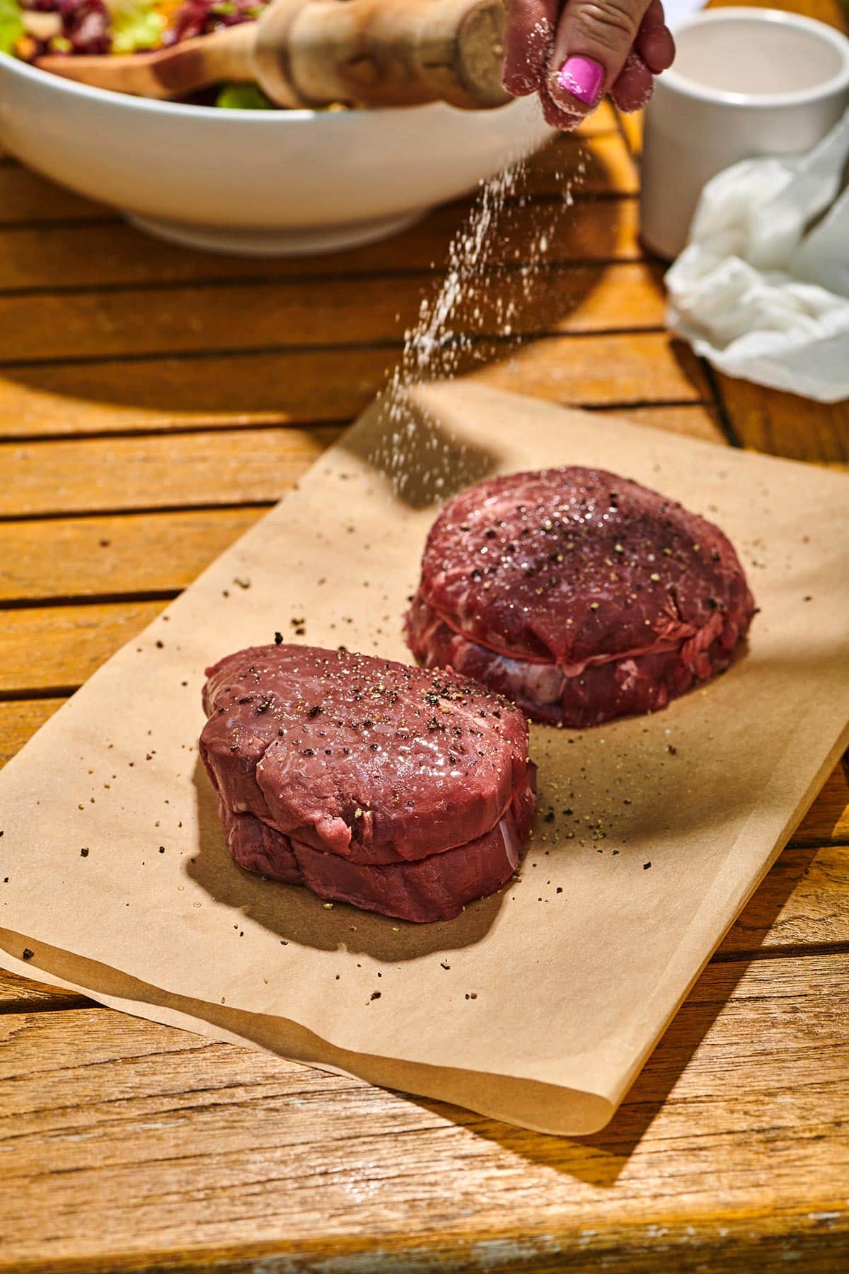 Seasoned raw filet mignon steaks on parchment paper outside.