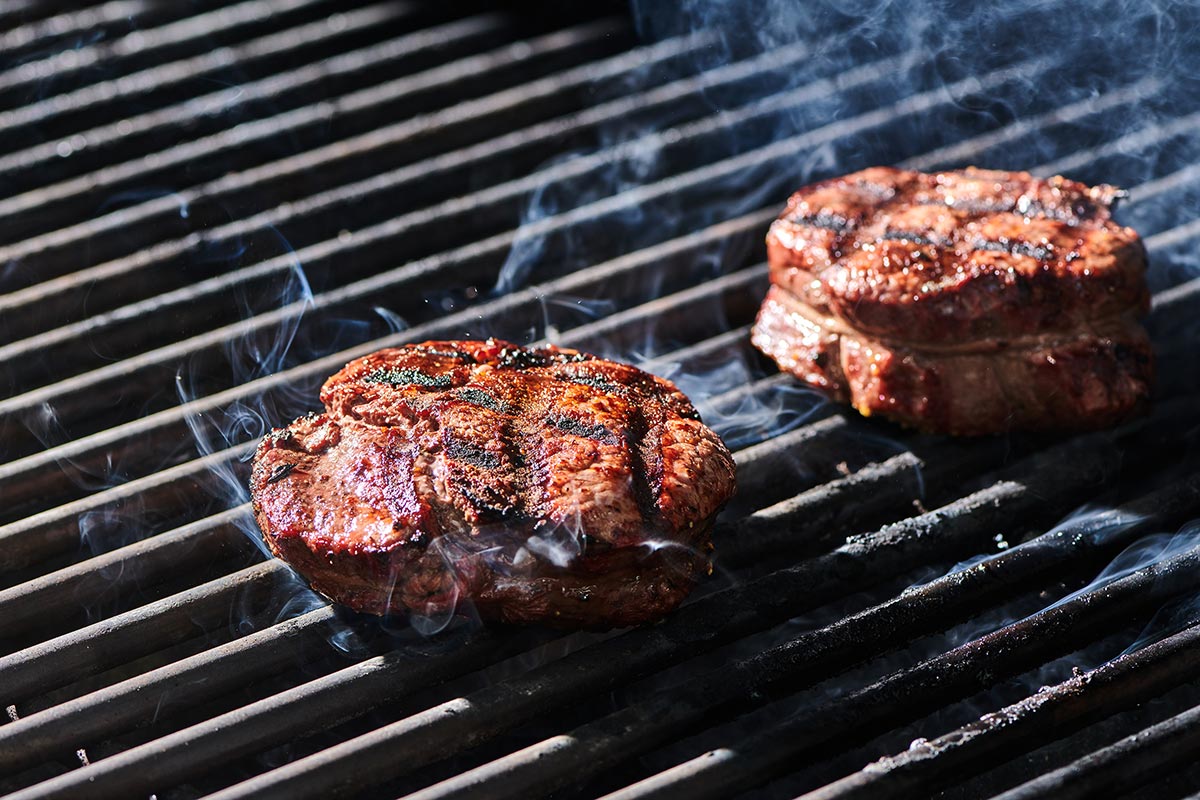 Round filet mignon steaks cooking on hot, smoky grill.