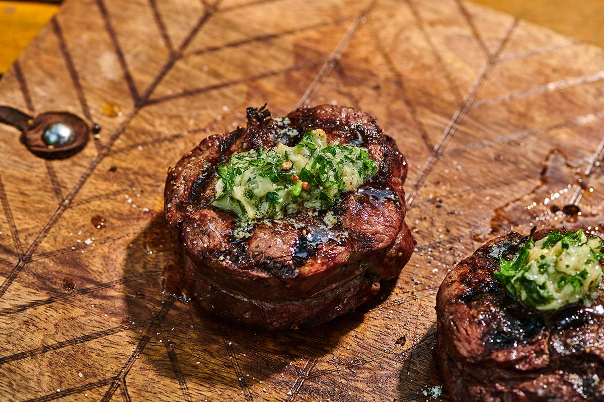 Grilled filet mignon steaks with dollop of garlic-parmesan compound butter on cutting board.