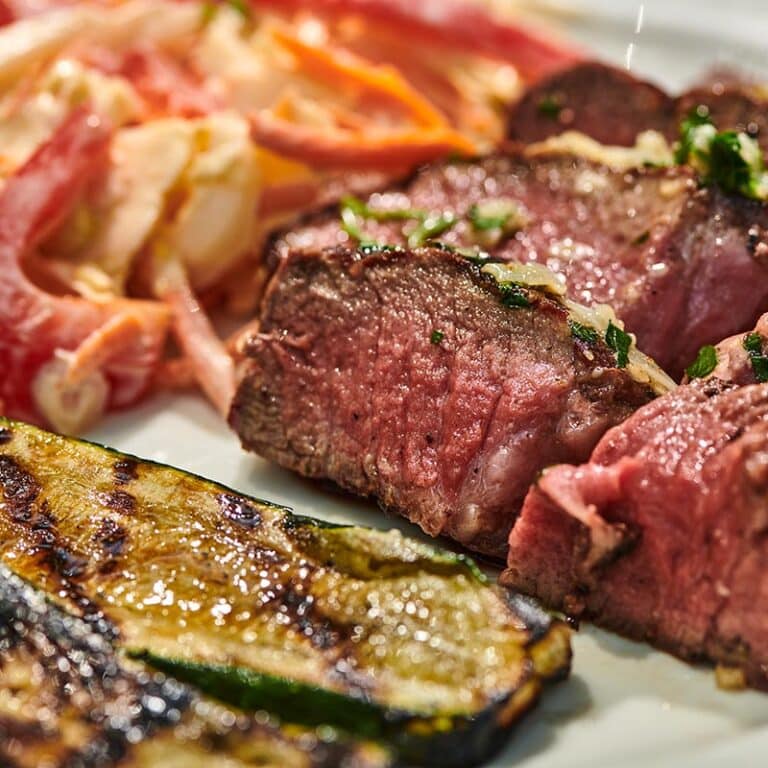 Slices of grilled filet mignon on plate with veggie sides.