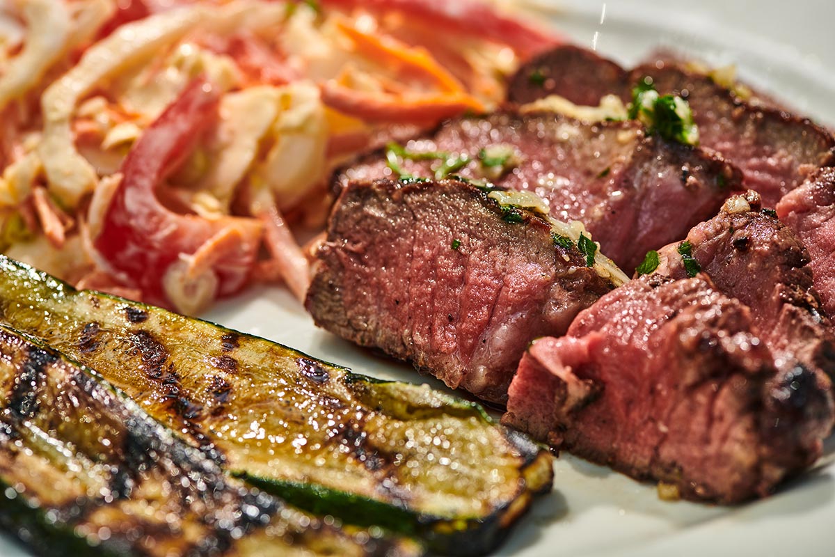 Slices of grilled filet mignon on plate with veggie sides.