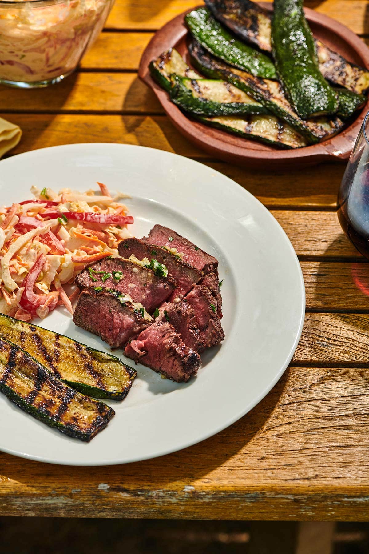 Slices of grilled filet mignon on picnic table with sides of grilled eggplant, cole slaw, and other sides.