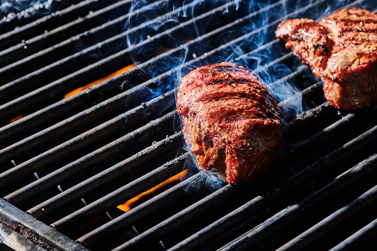 Grilling ranch steaks on smoking-hot barbecue grates.