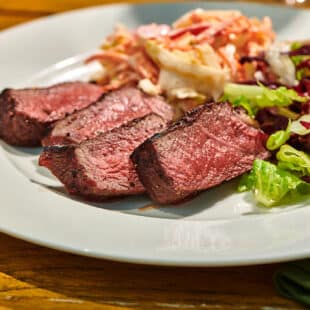 Slices of grilled ranch steaks on plate with leafy salad.