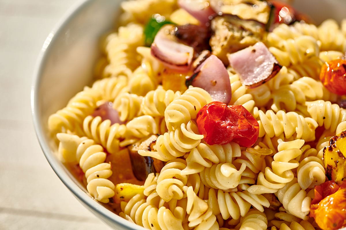 Pasta salad with rotini and grilled vegetables in white bowl.