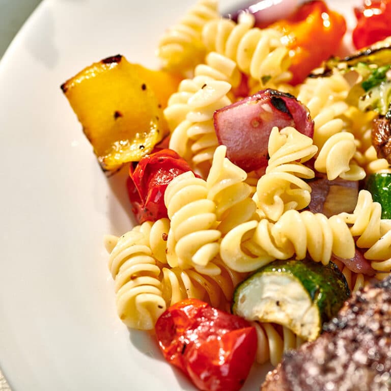 Pasta salad with grilled veggies in white bowl.
