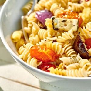 White bowl at picnic filled with pasta salad featuring grilled veggies.