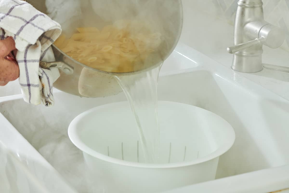 Draining ziti pasta into colander in sink.