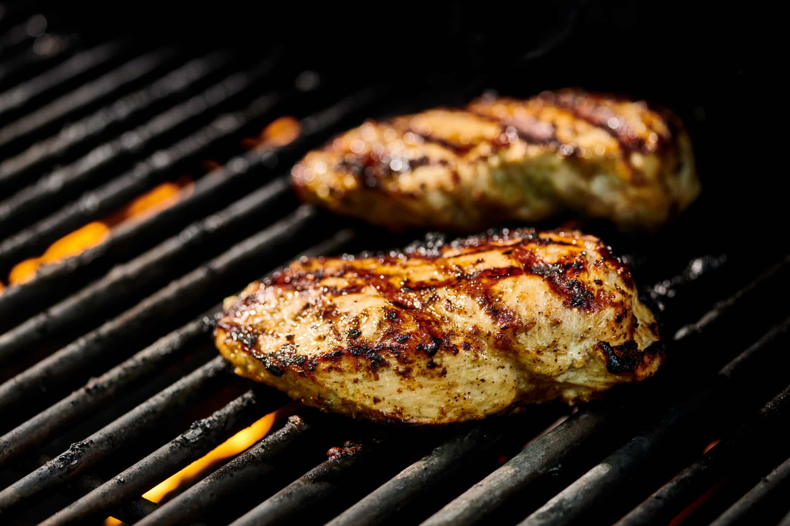 Marinated chicken breasts cooking over flames on hot grill.