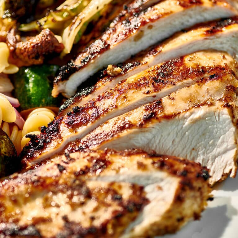 Sliced Jamaican jerk chicken breasts on plate with veggie sides.