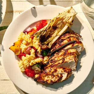 Outdoor table setting with plate of grilled Jamaican jerk-style chicken breasts and veggies.