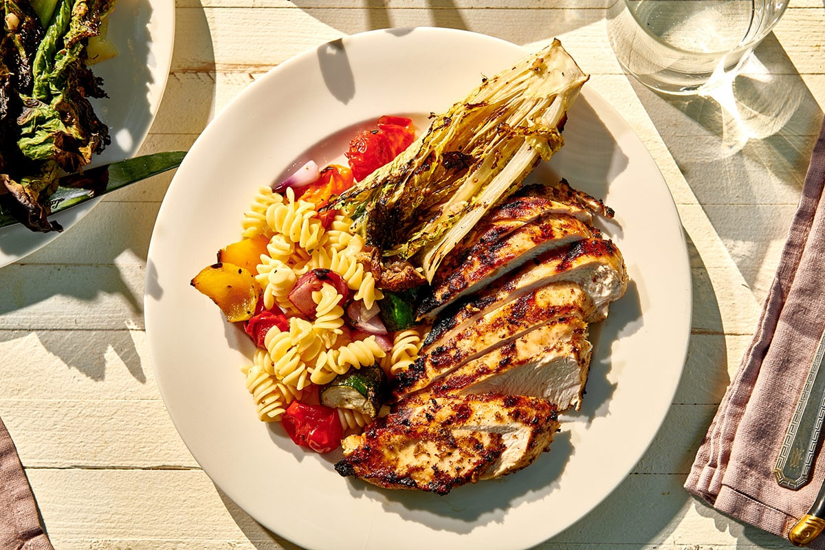 Outdoor table setting with plate of grilled Jamaican jerk-style chicken breasts and veggies.