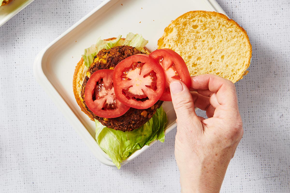 Woman placing sliced tomatoes on black bean burger.
