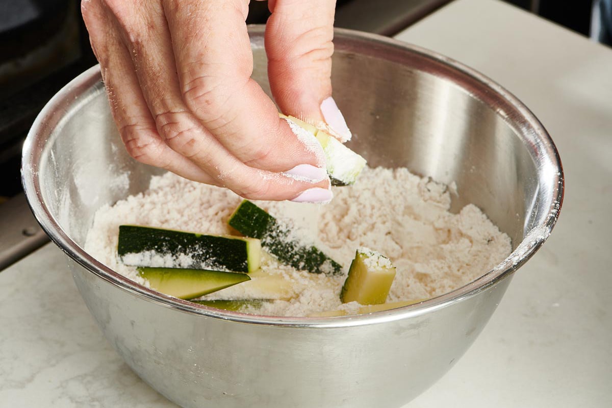 Woman dipping zucchini sticks in bowl of beer and flour batter.