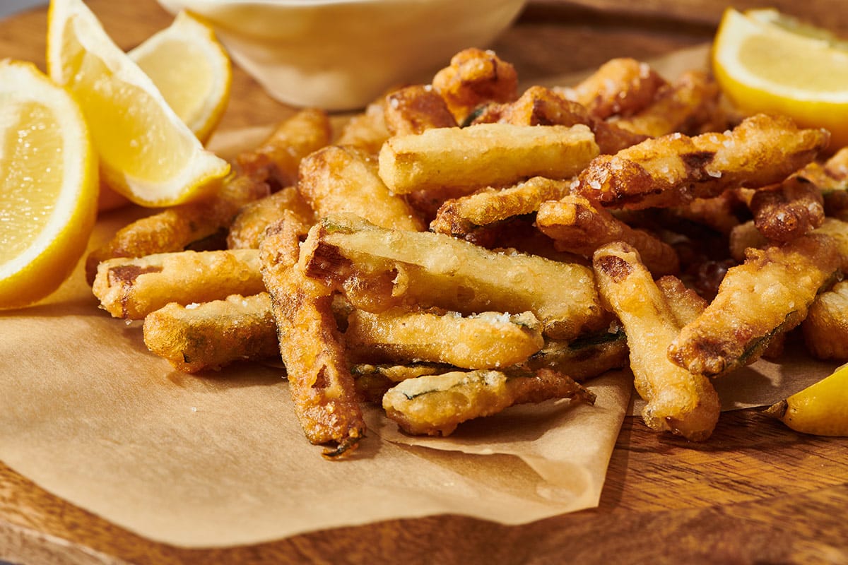 Freshly cooked zucchini fries on paper with lemon wedges.