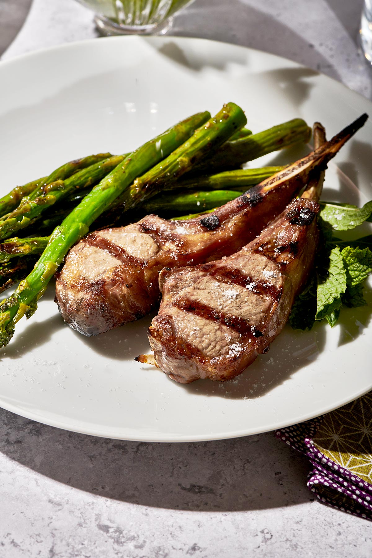 Grilled Rib Lamb Chops on white plate with grilled asparagus.