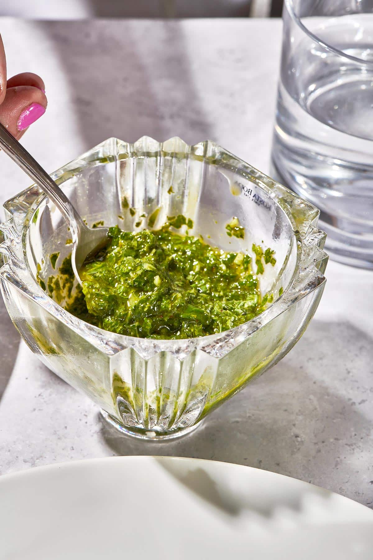 Scooping mint-basil pesto out of glass dish with spoon.