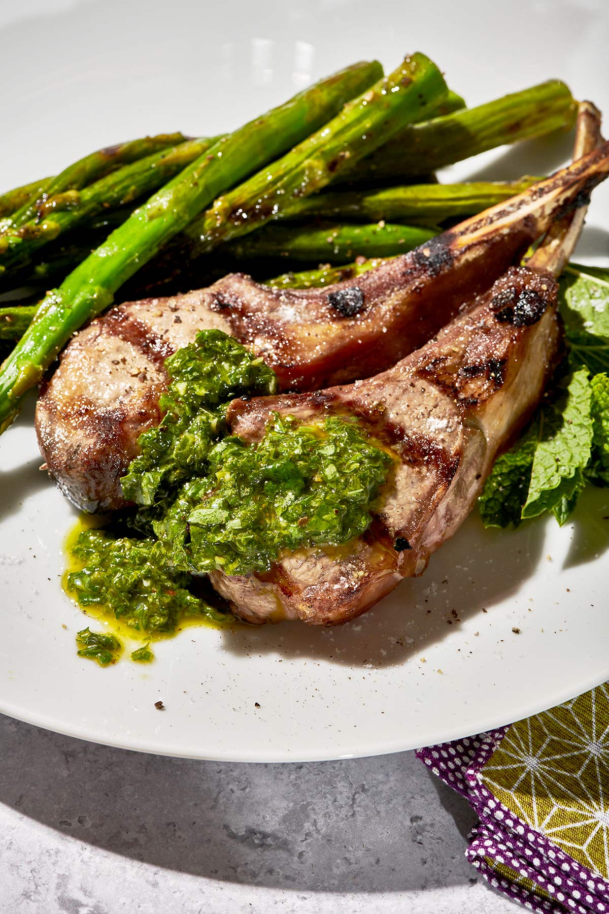 Picnic table with plate of Grilled Rib Lamb Chops covered in pesto alongside asparagus.