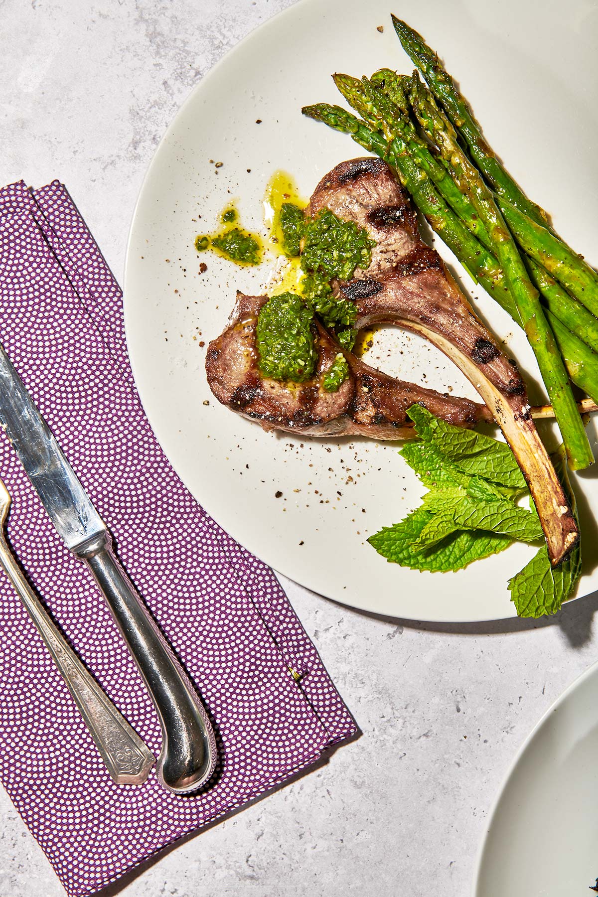 Picnic table with plated grilled rib lamb chops and asparagus next to purple napkin.
