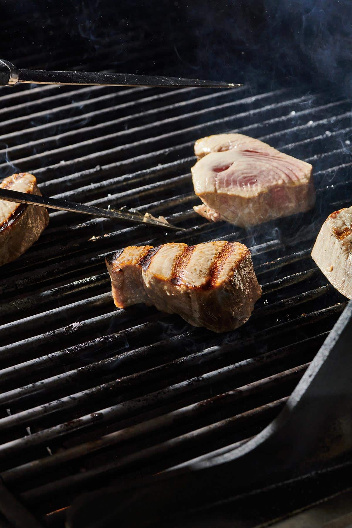 Flipping tuna steaks on grill with tongs.