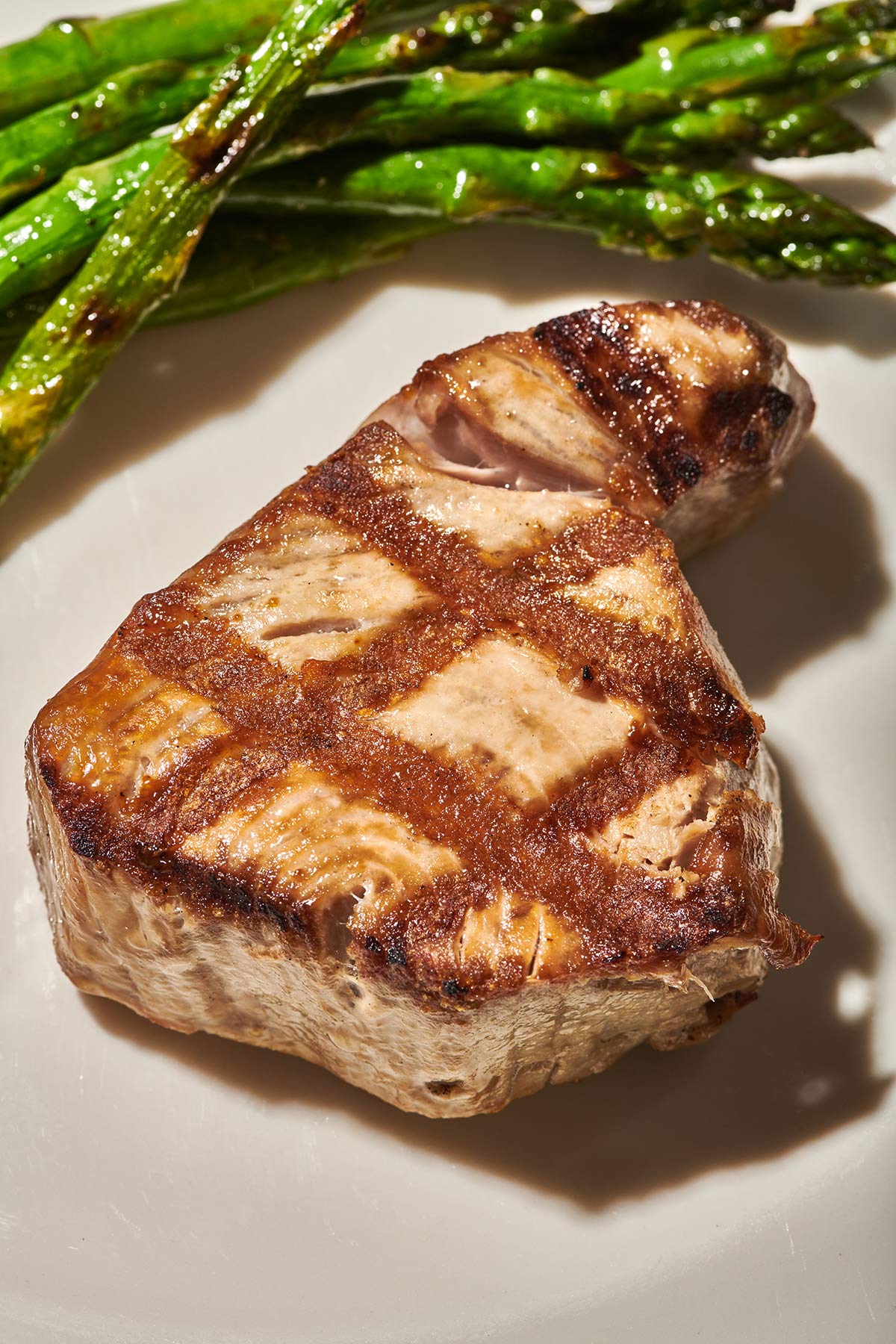Grilled tuna steak on plate next to asparagus.