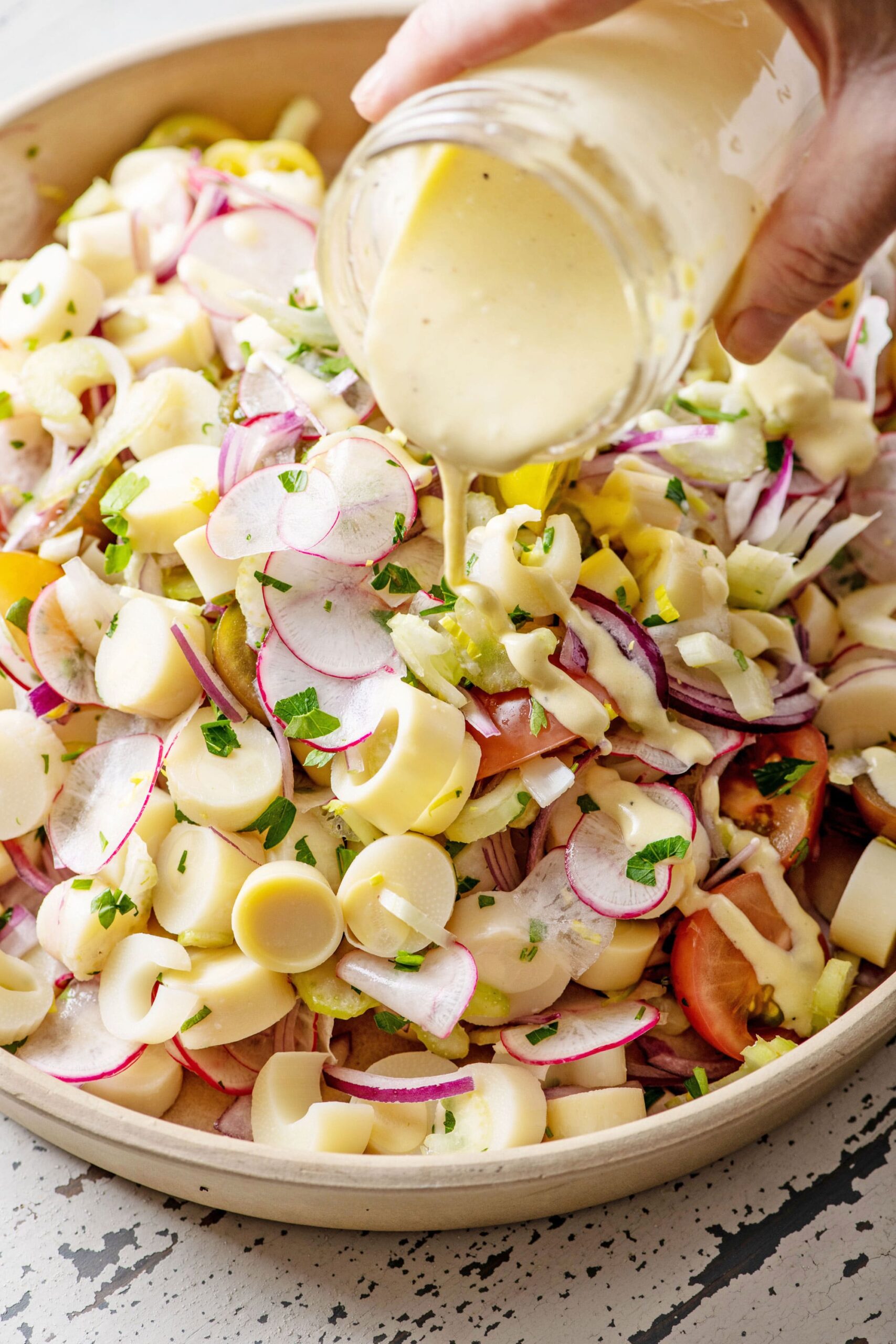 Pouring dressing from a jar over Hearts of Palm Salad in bowl.