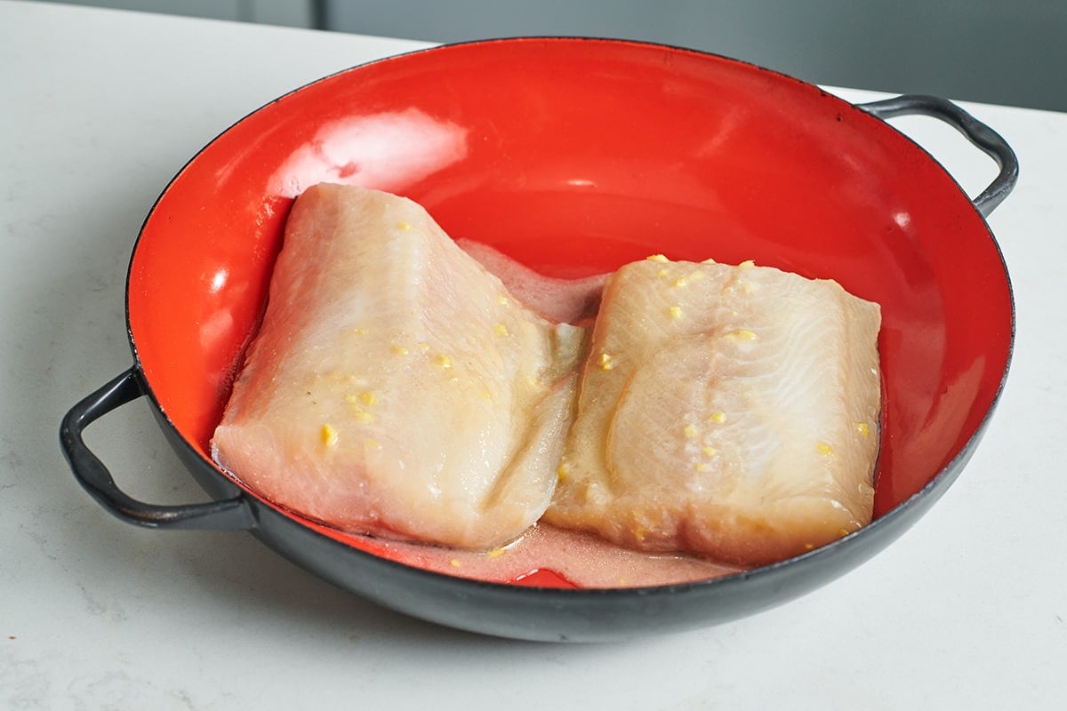 Cod filets marinating in red and black bowl.