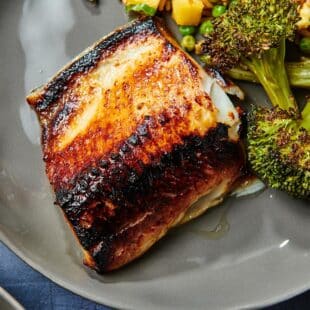 Broiled cod with miso glaze on plate with sauteed broccoli.