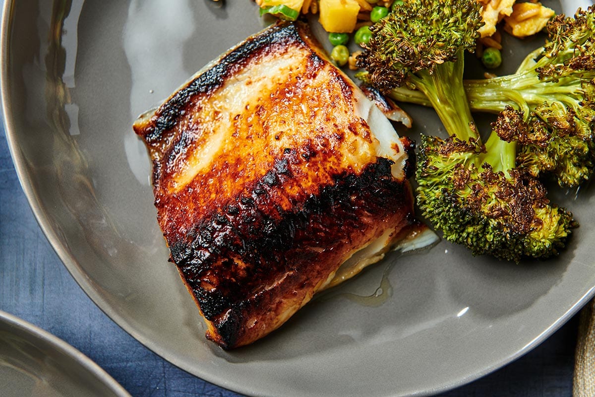 Broiled cod with miso glaze on plate with sauteed broccoli.