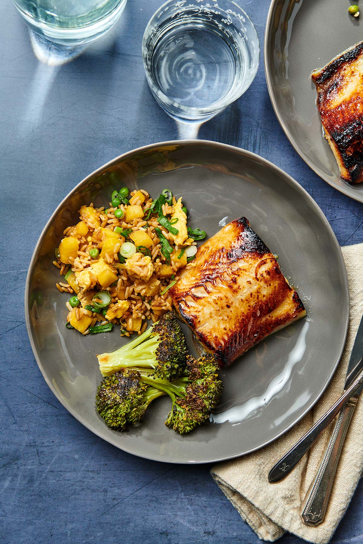 Plate on table with miso black cod, broccoli, and fried rice.
