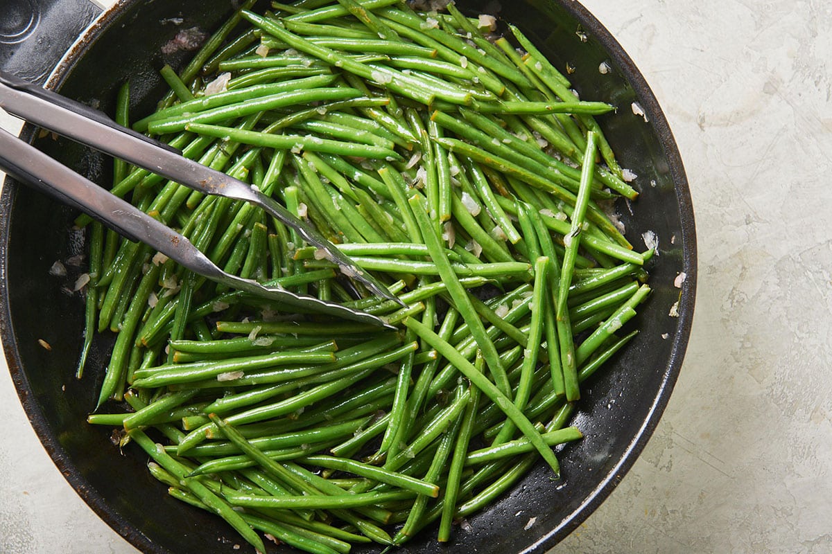 Tongs in a skillet of Sautéed Green Beans with Thyme Butter.