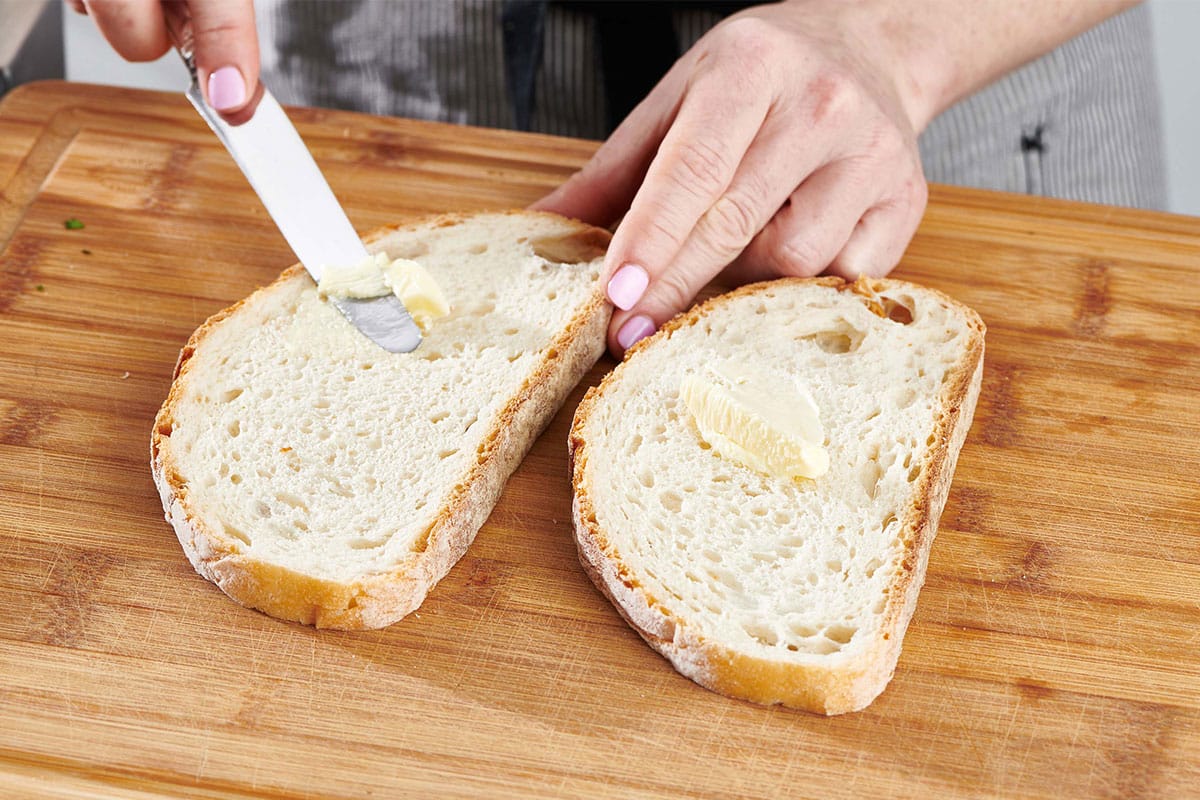 Woman buttering bread on a wooden cutting board.