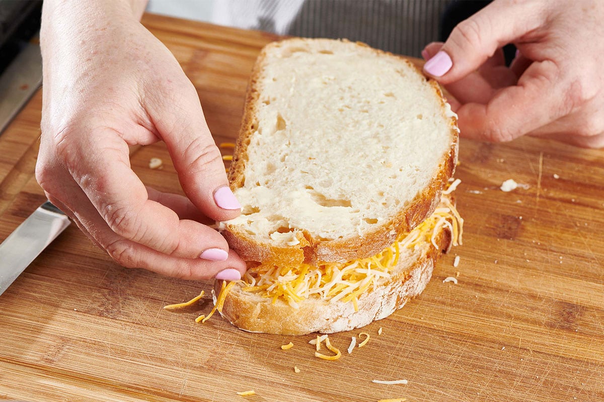 Woman assembling grilled cheese sandwich on a wooden cutting board.