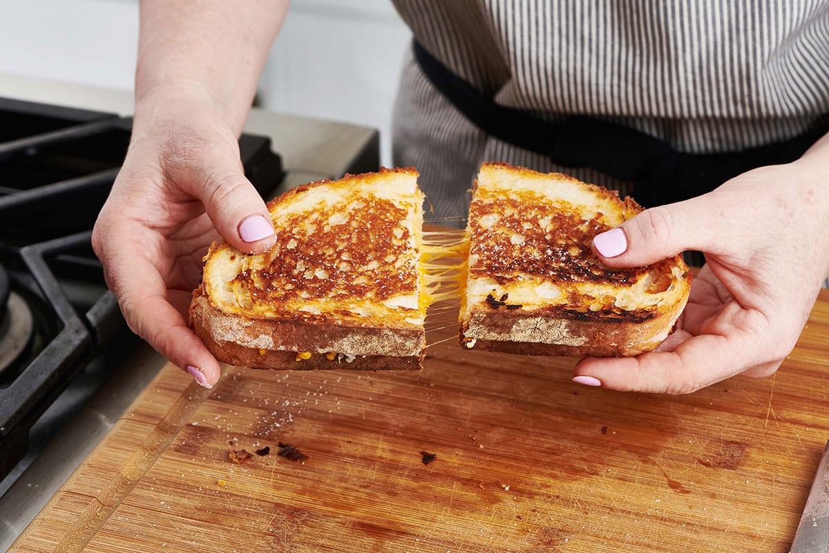 Woman pulling apart a warm grilled cheese sandwich cut in half.
