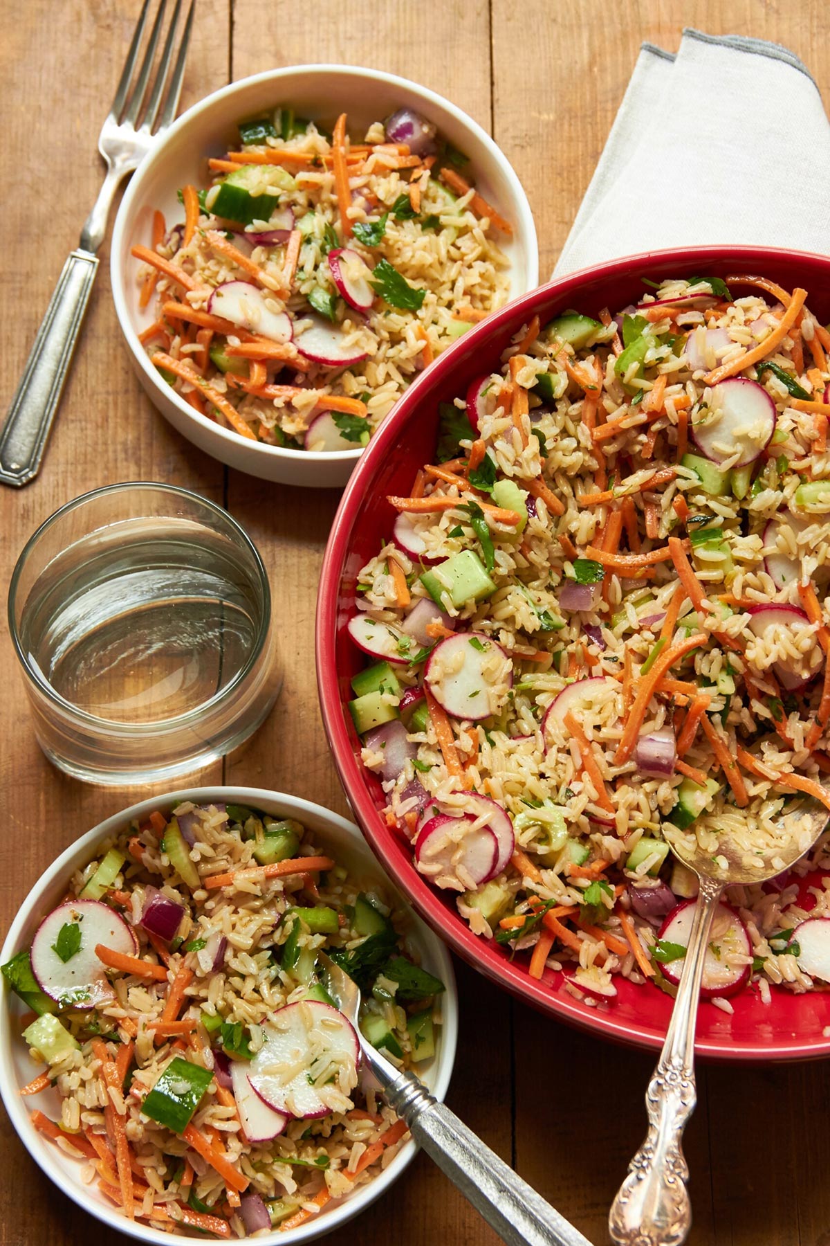 Table set with bowls of brown rice and veggie salad with water.