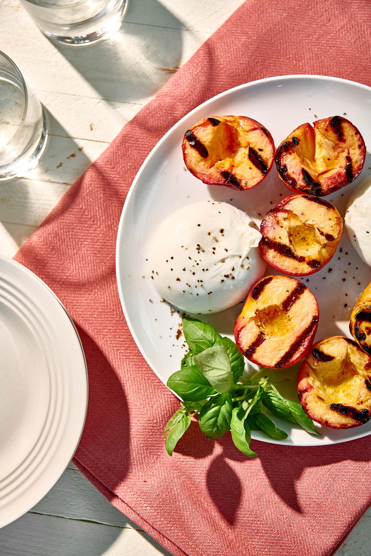 Mound of burrata cheese with grilled peaches on picnic plate.