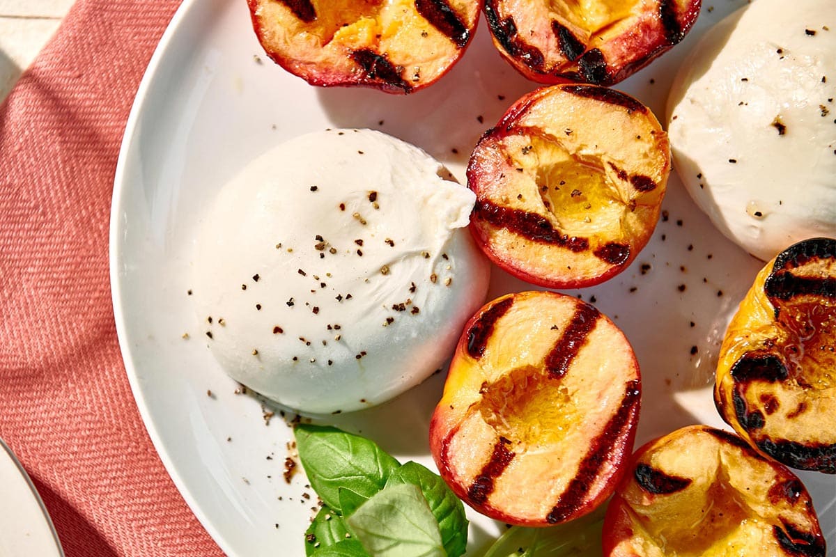 Grilled peaches, burrata cheese, and fresh basil on plate.