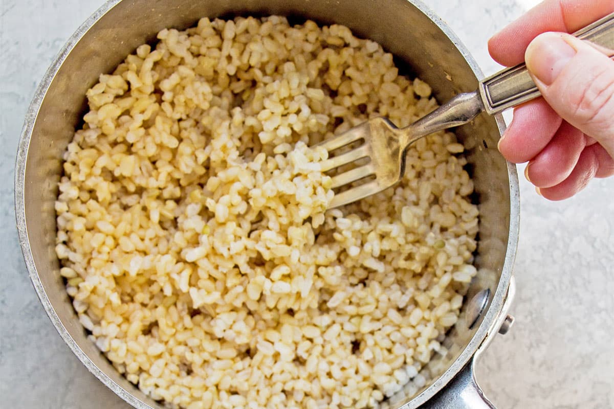 Fluffing cooked brown rice in pot with fork.