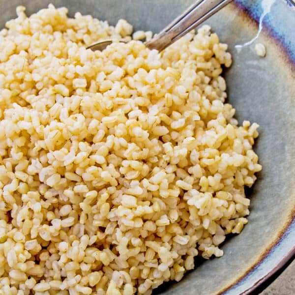 Cooked brown rice in grey bowl with fork.