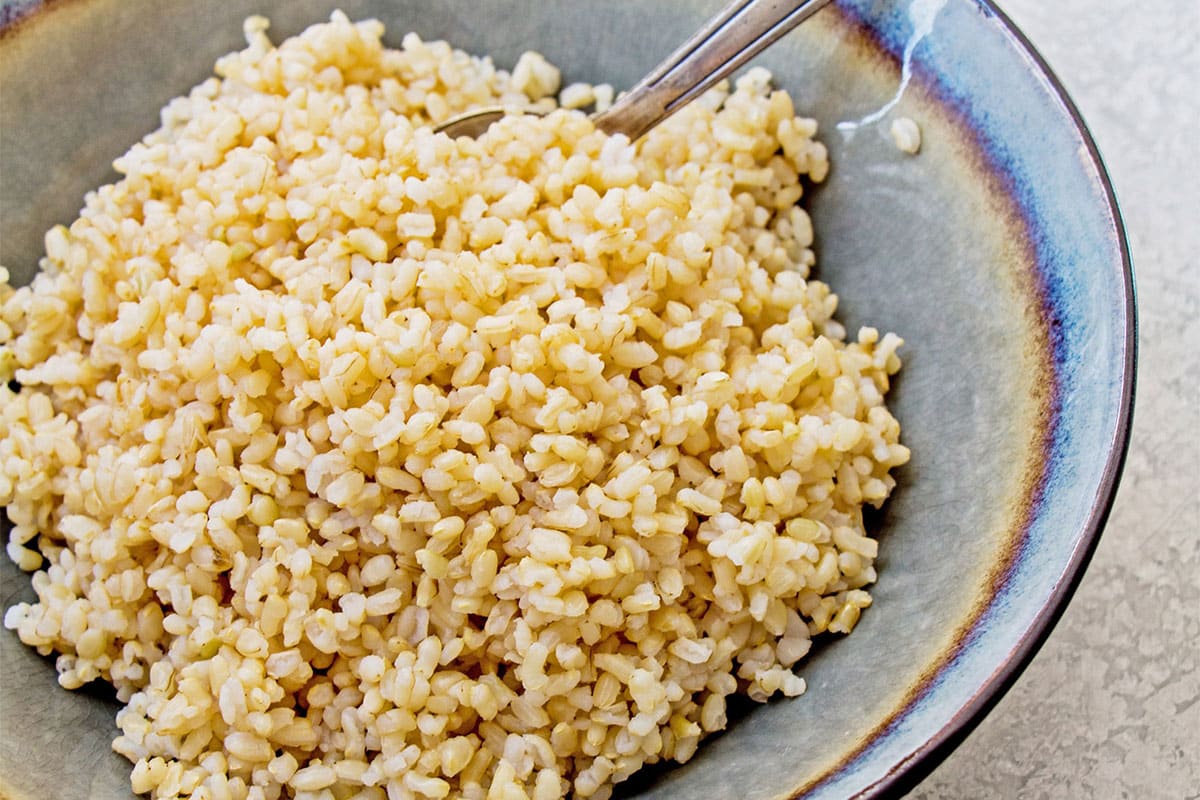 Cooked brown rice in grey bowl with fork.