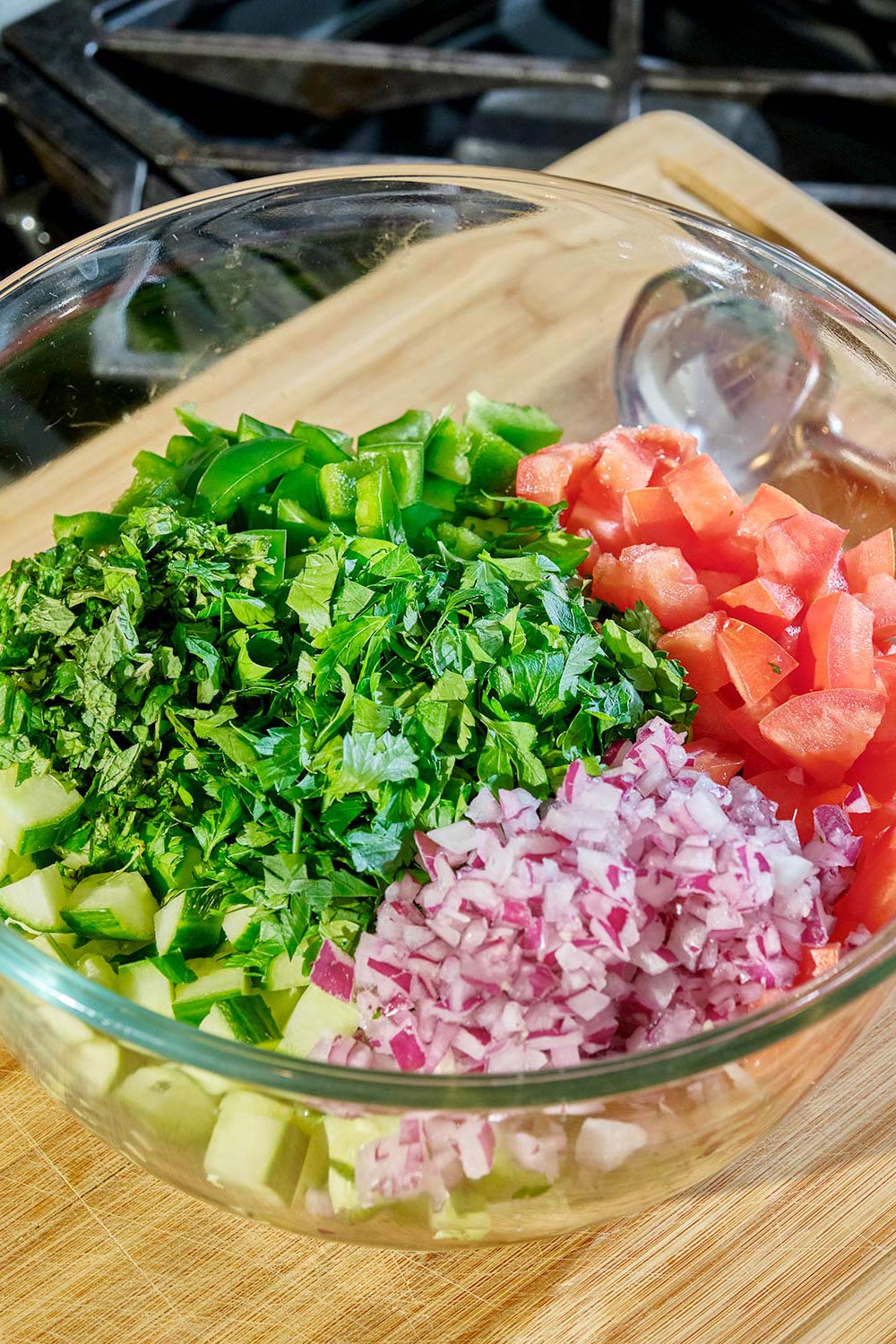 Chopped tomatoes, cucumber, bell pepper, and red onion in glass bowl.